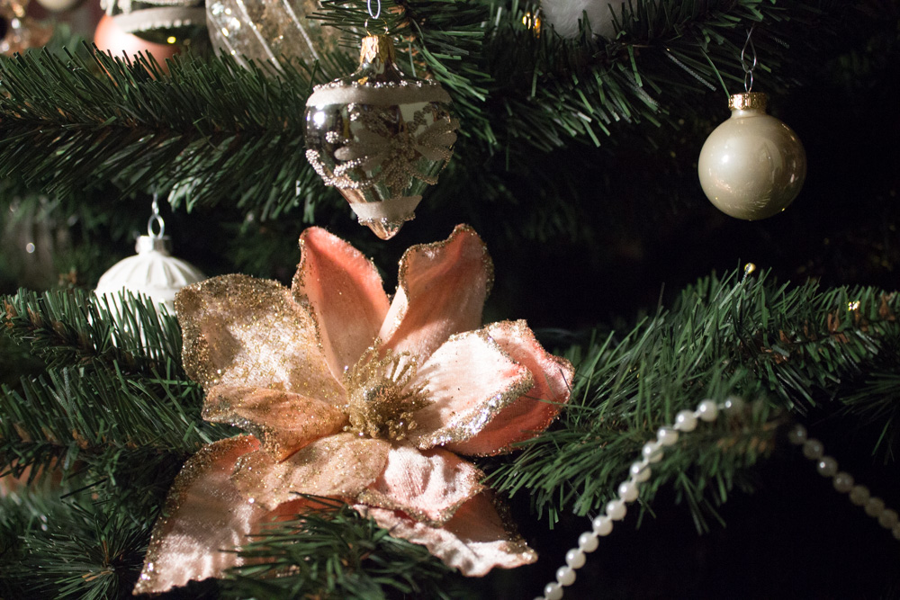 Detail of the Christmas tree with a peach-colored flower in gold glitter. Silver handmade heart bauble with white micro-beads and beige bauble.