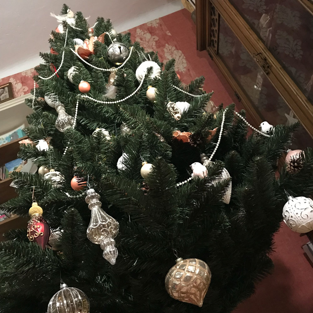 Christmas tree decorated with silver-clear, silver-white, golden and burgundy-gold baubles. Peach colored flowers and baubles, white feather birds and pearl strings.